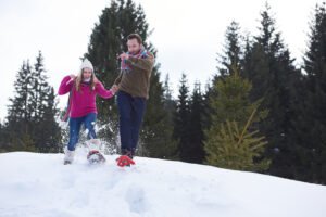 happy young couple having fun and walking in snow shoes outdoor in nature at beautiful winter day. Health sport and relaxation