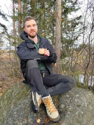 Guide sitting on the rock in Rovaniemi forest. Drinking from kuksa.